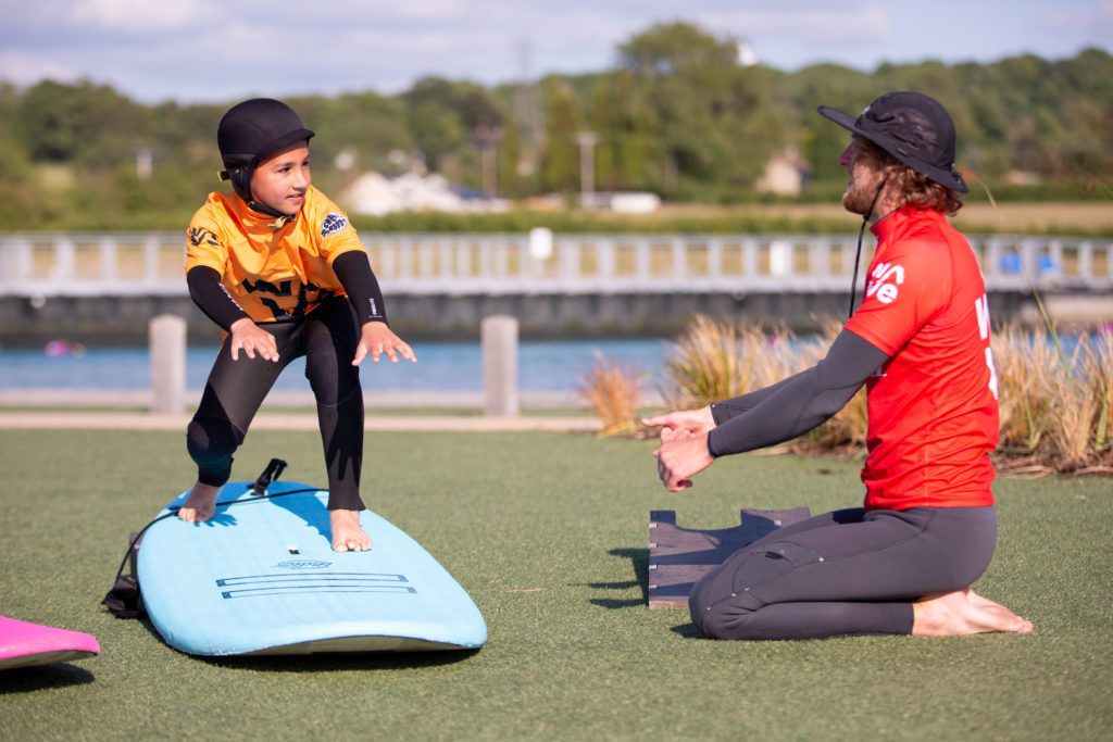 Coach teaches child manuouvers to pop-up on surfboard on dry land.